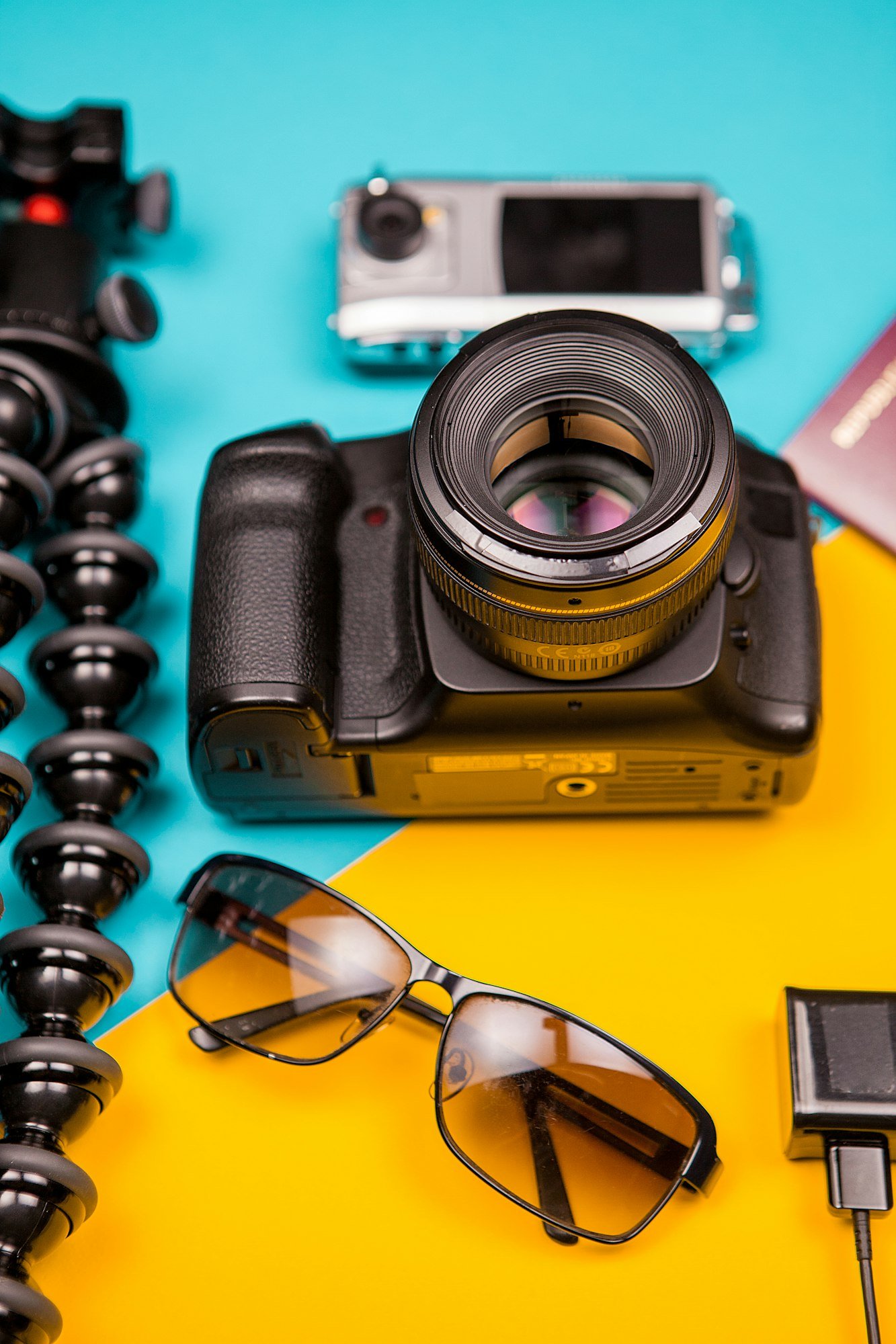 DSLR and action camera next to a tripod, sunglasses and passport